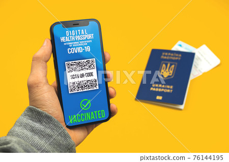 Person shows valid health passport app on mobile phone screen, background with ticket on a plane, travel during pandemic concept 76144195