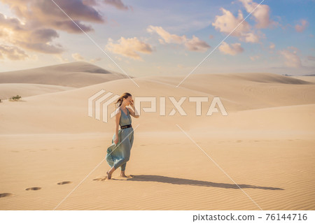 Young beautiful woman traveling in the desert. Sandy dunes and blue sky on sunny summer day. Travel, adventure, freedom concept. Tourism reopens after quarantine COVID 19 Young beautiful woman traveling in the desert. Sandy dunes and blue sky on sunny summer day. Travel, adventure, freedom concept. Tourism reopens after quarantine COVID 19 76144716