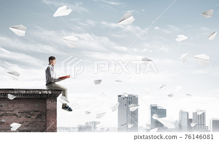 Handsome student guy on roof edge reading book and paper planes fly around 76146081