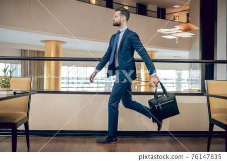 Buisnessman in a blue suit holding a suitcase walking fast Buisnessman in a blue suit holding a suitcase walking fast 76147835