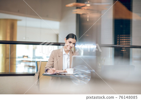 Young businesswoman in beige jacket sitting in the office in front of the laptop 76148085