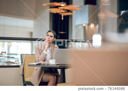 Young businesswoman in beige jacket sitting in the office in front of the laptop 76148086