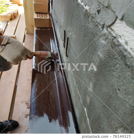 A man paints a metal corner with brown paint, working on a construction site. 76149325