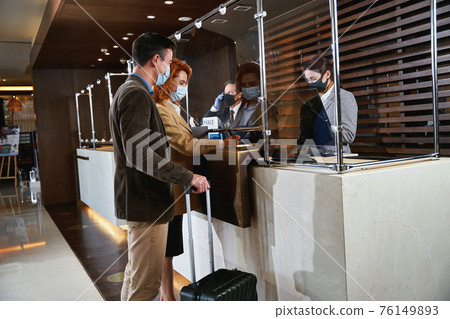 Guests filling in the registration form at the reception desk 76149893