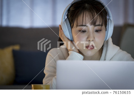 A woman wearing headphones and looking at a laptop screen A woman wearing headphones and looking at a laptop screen 76150635