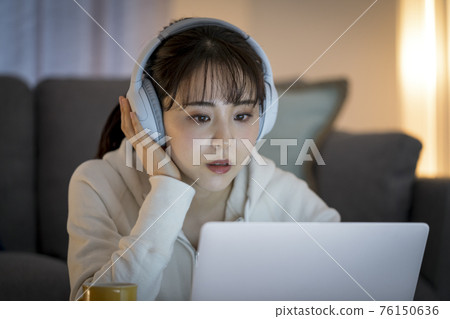 一個女人戴著耳機,看著筆記本電腦的屏幕 一個女人戴著耳機,看著筆記本電腦的屏幕 76150636