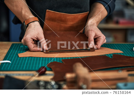 Skilled leather manufacture worker cutting some samples 76158164