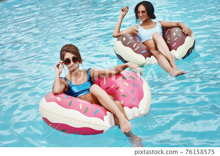Swimming is my sport, The pool is my Home, The water is my friend. Girls relaxing with inflatable rings in the shape of donuts 76158575
