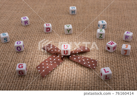 A ribbon and scattered dice-sized alphabet cubes on a textured surface A ribbon and scattered dice-sized alphabet cubes on a textured surface 76160414