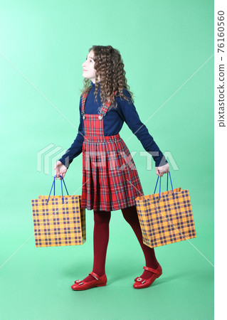 Child with a yellow packaging checkered texture  isolated on green background. Holiday present, shopping. 76160560