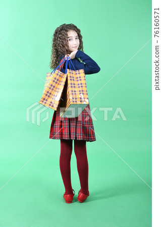 Child with a yellow packaging checkered texture  isolated on green background. Holiday present, shopping. 76160571