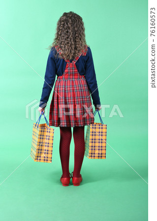 Child with a yellow packaging checkered texture  isolated on green background. Holiday present, shopping. 76160573