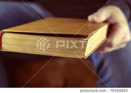 An outstretched hand with a book in close-up. 76160805