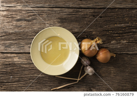 Bowl with clear rich broth. White crockery on an aged wooden table. Vegetables - onions, garlic, spices Bowl with clear rich broth. White crockery on an aged wooden table. Vegetables - onions, garlic, spices 76160879