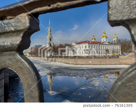 St. Nicholas Naval Cathedral belltower through the forged lattice in a clear sunny day of spring, an ice drift on Kryukov and Griboyedov Canal, a view of seven bridges from the embankment 76161305