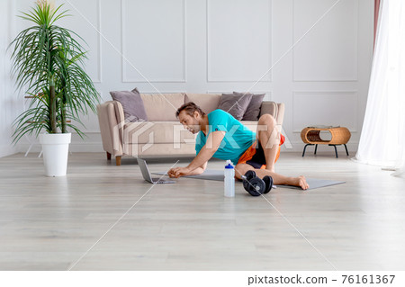 Man is watching a tutorial on training at home. He lies on the floor at home in front of a laptop monitor. Healthy lifestyle concept. Man is watching a tutorial on training at home. He lies on the floor at home in front of a laptop monitor. Healthy lifestyle concept. 76161367
