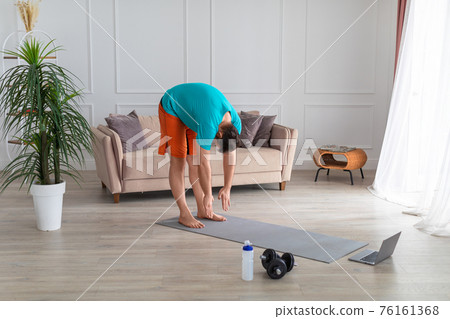 Man during stretching workout at home in front of laptop monitor. Man during stretching workout at home in front of laptop monitor. 76161368