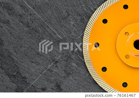 Half of a yellow diamond cutting wheel with a threaded nut on a dark gray granite background, the concept of stone processing in the interior and construction. 76161467
