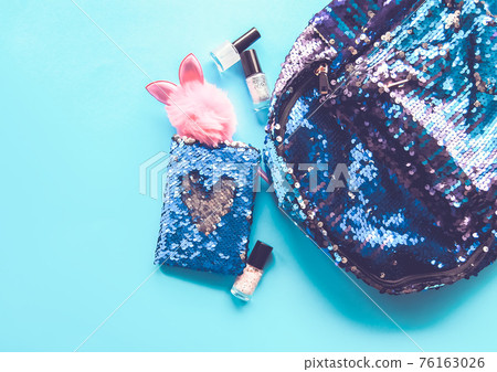 Bright composition of fashion accessories. Glitter sequins backpack, notepad, funny pen, nail polish. Different objects on soft pastel background. Flat lay, top view Bright composition of fashion accessories. Glitter sequins backpack, notepad, funny pen, nail polish. Different objects on soft pastel background. Flat lay, top view 76163026
