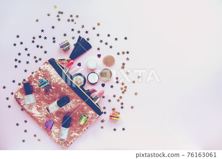 Bright composition of fashion accessories. Glitter sequins cosmetic bag with lipsticks, nail polishes and other objects. Object on soft pastel background with decorative tinsel. Flat lay, top view. Bright composition of fashion accessories. Glitter sequins cosmetic bag with lipsticks, nail polishes and other objects. Object on soft pastel background with decorative tinsel. Flat lay, top view. 76163061