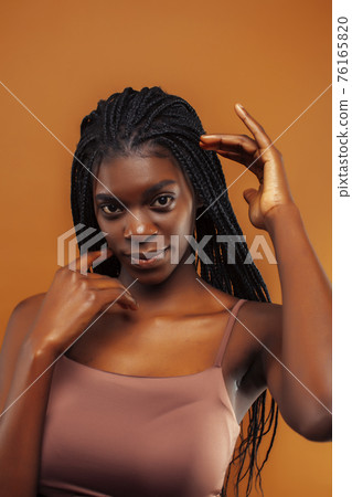 pretty young african american woman with braids posing cheerful gesturing on brown background, lifestyle people concept 76165820