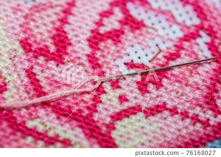 Close-up on a sewing needle with a thread lying on top of cross-stitched canvas Close-up on a sewing needle with a thread lying on top of cross-stitched canvas 76168027