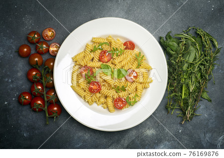 Food pasta on a dark background. Italian fusilli pasta with tomatoes, herbs and basil on a white plate. Healthy food concept. 76169876