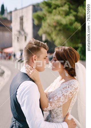 Portrait of a wedding couple on the street, the bride hugs the groom by the neck, the groom hugs her around the waist. Fine-art wedding photo in Montenegro, Perast.  76170999