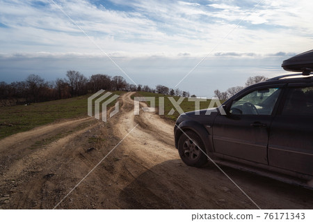 A gravel road leading toward horizon. Spectacular view on the sea and blue sky in the evening. Offroad 4x4 car 76171343