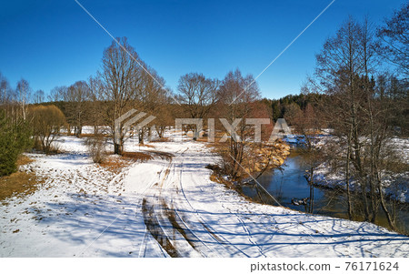 Early spring landscape with melting snow. Dirt rural road, wood, ice and snow panorama. Early spring landscape with melting snow. Dirt rural road, wood, ice and snow panorama. 76171624