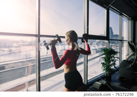 Coronavirus covid-19 prevention, fitness girl with a medical mask holding a dumbbell . Fighting viruses. 76172296