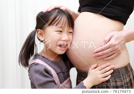 足月的媽媽和女兒聽到腹部的胎兒運動 足月的媽媽和女兒聽到腹部的胎兒運動 76174873