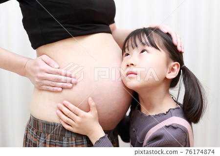 足月的媽媽和女兒聽到腹部的胎兒運動 足月的媽媽和女兒聽到腹部的胎兒運動 76174874