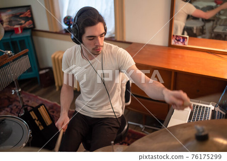 Young man with headphones plays drums in home music room Young man with headphones plays drums in home music room 76175299