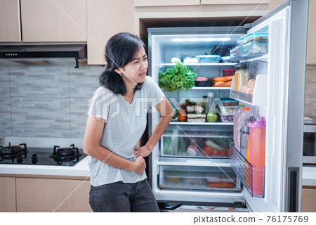starving young asian woman hold her belly while open the fridge door looking for food starving young asian woman hold her belly while open the fridge door looking for food 76175769