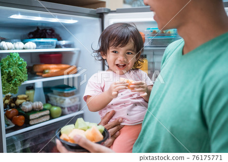 father and daughter open refrigerator at home having some fresh fruit together father and daughter open refrigerator at home having some fresh fruit together 76175771