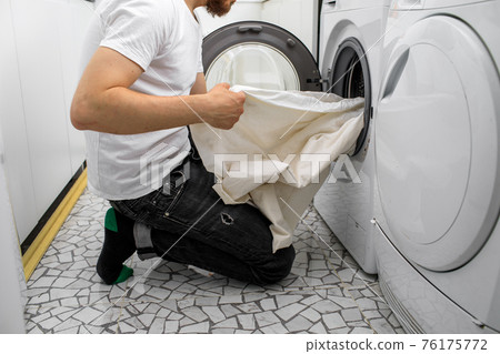man puts laundry in a washing machine 76175772