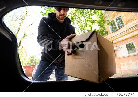 young man puts a box in the trunk of a car inside view young man puts a box in the trunk of a car inside view 76175774