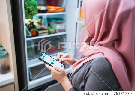 woman using her smartphone to buy groceries while open her fridge woman using her smartphone to buy groceries while open her fridge 76175779