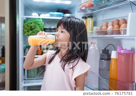 asian girl open fridge door drinking a bottle of juice asian girl open fridge door drinking a bottle of juice 76175781