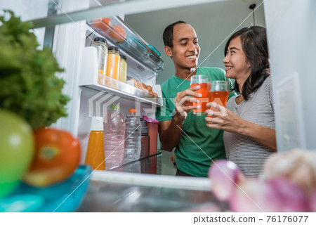 couple having a glass of juice in front of the open fridge couple having a glass of juice in front of the open fridge 76176077