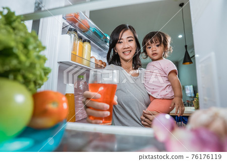 mother carrying her daughter while taking a glass of juice inside the fridge mother carrying her daughter while taking a glass of juice inside the fridge 76176119