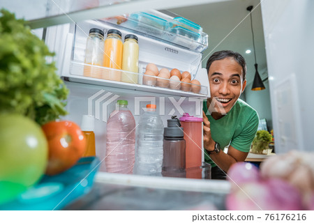 excited young asian man opening the fridge door excited young asian man opening the fridge door 76176216