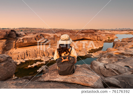 Explorer woman sitting on natural rock canyon at evening in Sam Phan Bok Explorer woman sitting on natural rock canyon at evening in Sam Phan Bok 76176392