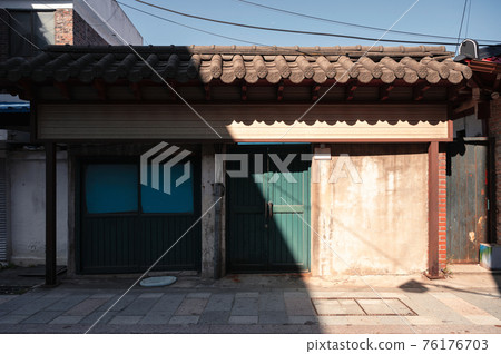 Sunlight shining on traditional house with green door and brick roof in alley 76176703