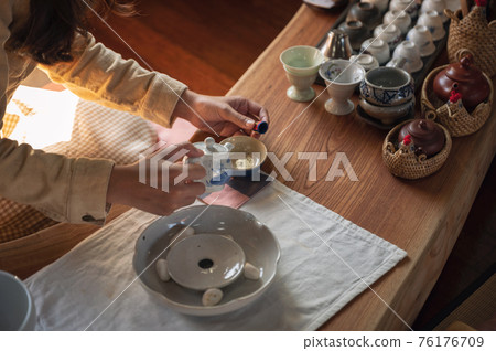 Woman hands pouring tea from teapot in a teacup on wood table 76176709