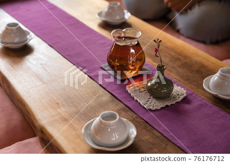 Hot tea in glass teapot with flower in vase and cup on wood table Hot tea in glass teapot with flower in vase and cup on wood table 76176712