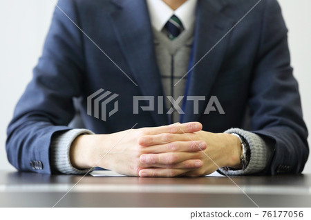 The front of the upper body of a man in a suit with his hands folded on the table 76177056