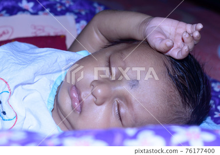 Close up face of a cute sleeping newborn baby. Closeup portrait of a Sweet just born infant boy captured in sleepy mood drowsy eyes. Hand on Head. Front view. Child care kid background image. Close up face of a cute sleeping newborn baby. Closeup portrait of a Sweet just born infant boy captured in sleepy mood drowsy eyes. Hand on Head. Front view. Child care kid background image. 76177400