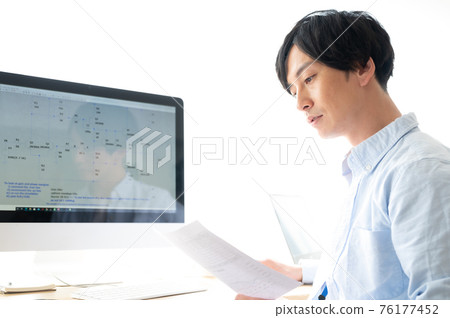 Male electrical engineer thinking while reading documents in front of a personal computer 76177452